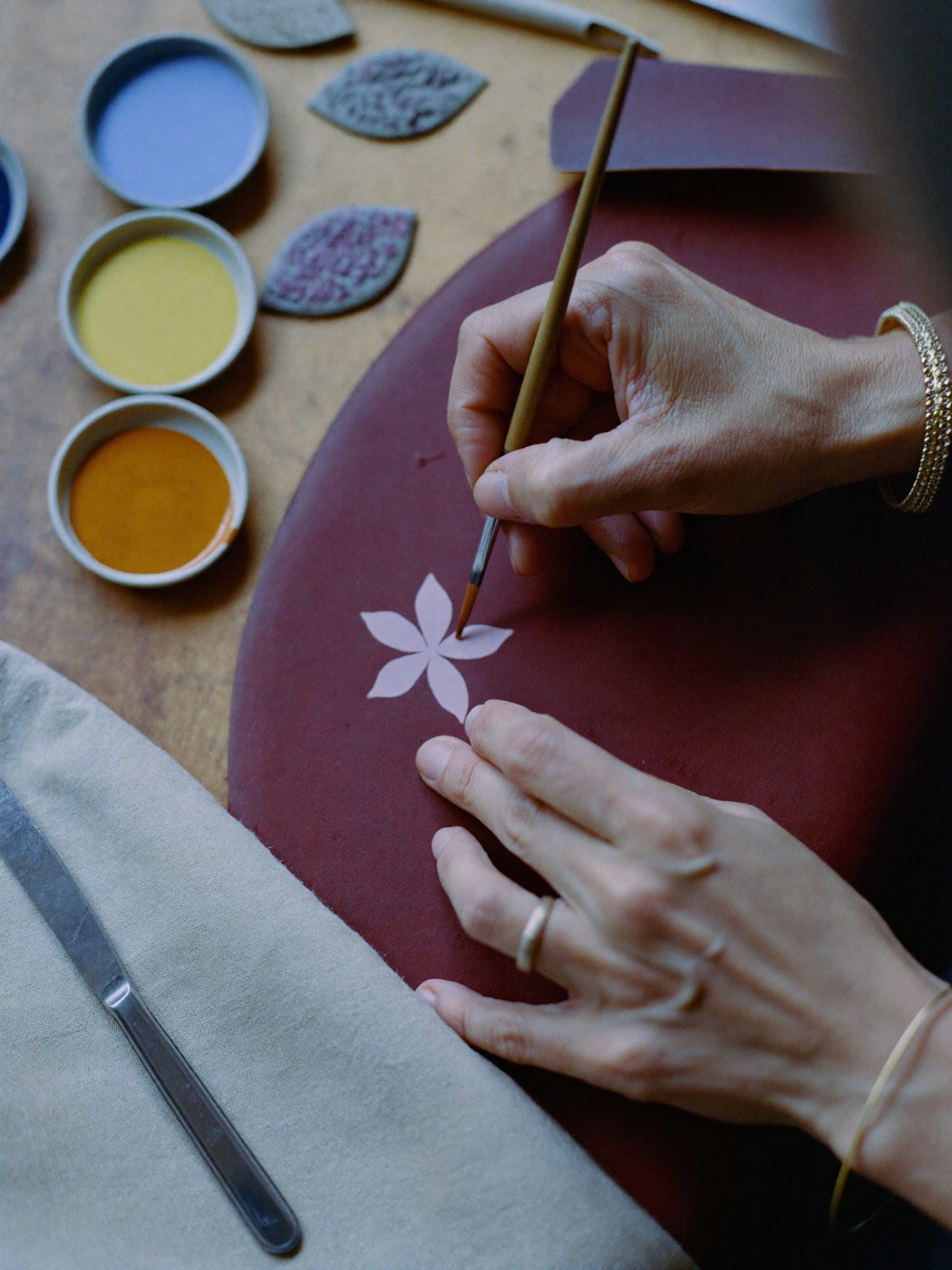 Hand-painting a Persian flower onto burgundy leather at the bench