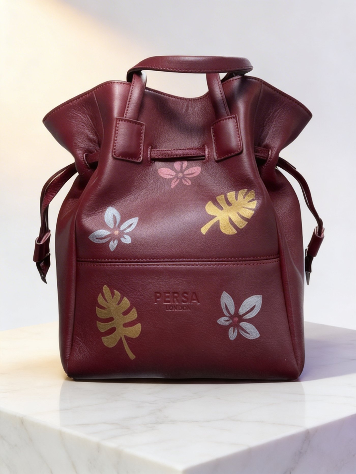 Hand-painted Persa London bucket bag on a stone plinth in editorial light